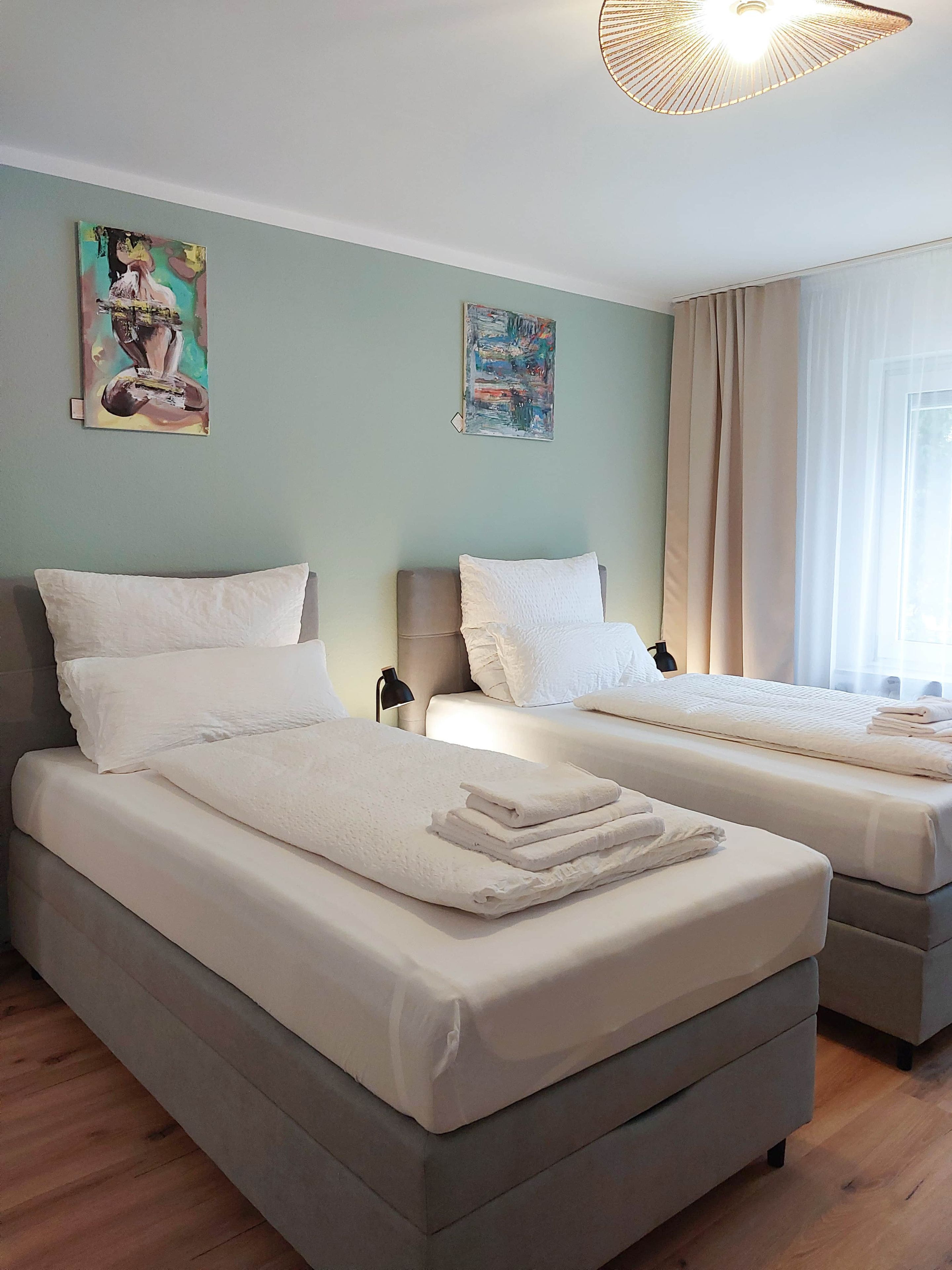 Ein Hotelzimmer mit zwei Betten, einem großen Fenster mit Vorhängen und Bildern an den Wänden.