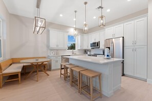 A modern kitchen with white cabinetry, a central island, bar stools, pendant lighting, and a view of the outdoors. - Sandpiper Shores (Fort Myers Beach)