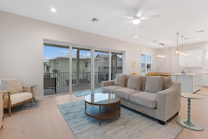 A modern living room with a sofa, a coffee table, and a view of a balcony. - Sandpiper Shores (Fort Myers Beach)