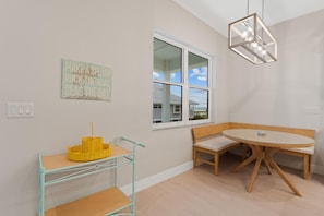 A room with a dining table, bench, wicker chair, and a wall-mounted light fixture. - Sandpiper Shores (Fort Myers Beach)
