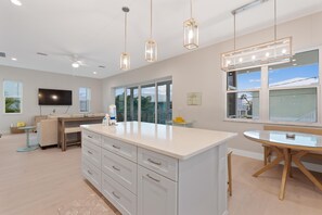A modern kitchen with a central island, pendant lights, and a dining area with a round table. - Sandpiper Shores (Fort Myers Beach)