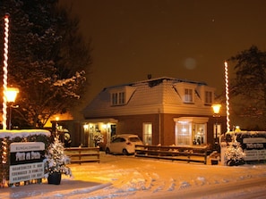 A bungalow with a snow-covered driveway, a car parked in front, and a sign indicating holidayhouses for rent. - de Mooij Family 2 (Noordwijk)