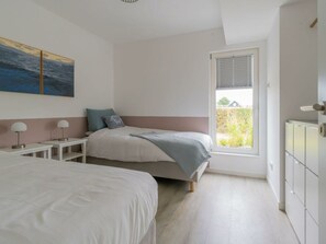 A bedroom with two beds, a window with blinds, a bedside table with a lamp, and a wall-mounted radiator. - Holiday Home in Renesse With Swimming Pool (Renesse)