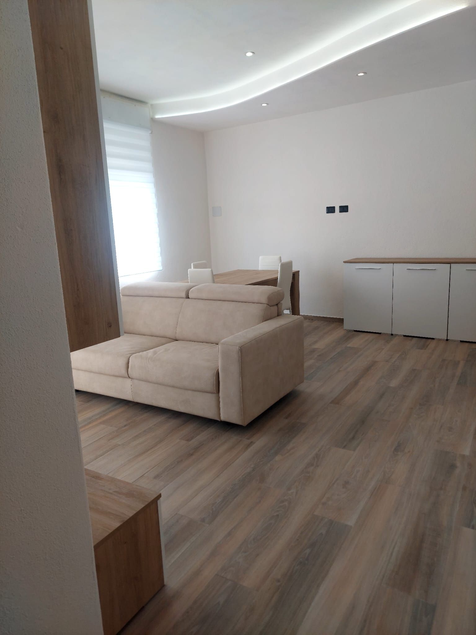 Una sala moderna con un sofá, un comedor con una mesa y una cocina con alacenas.