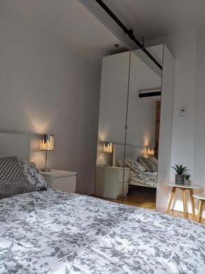Ein Schlafzimmer mit einem Bett, Nachttischen, einem Spiegel und einem kleinen Tisch mit einer Pflanze.