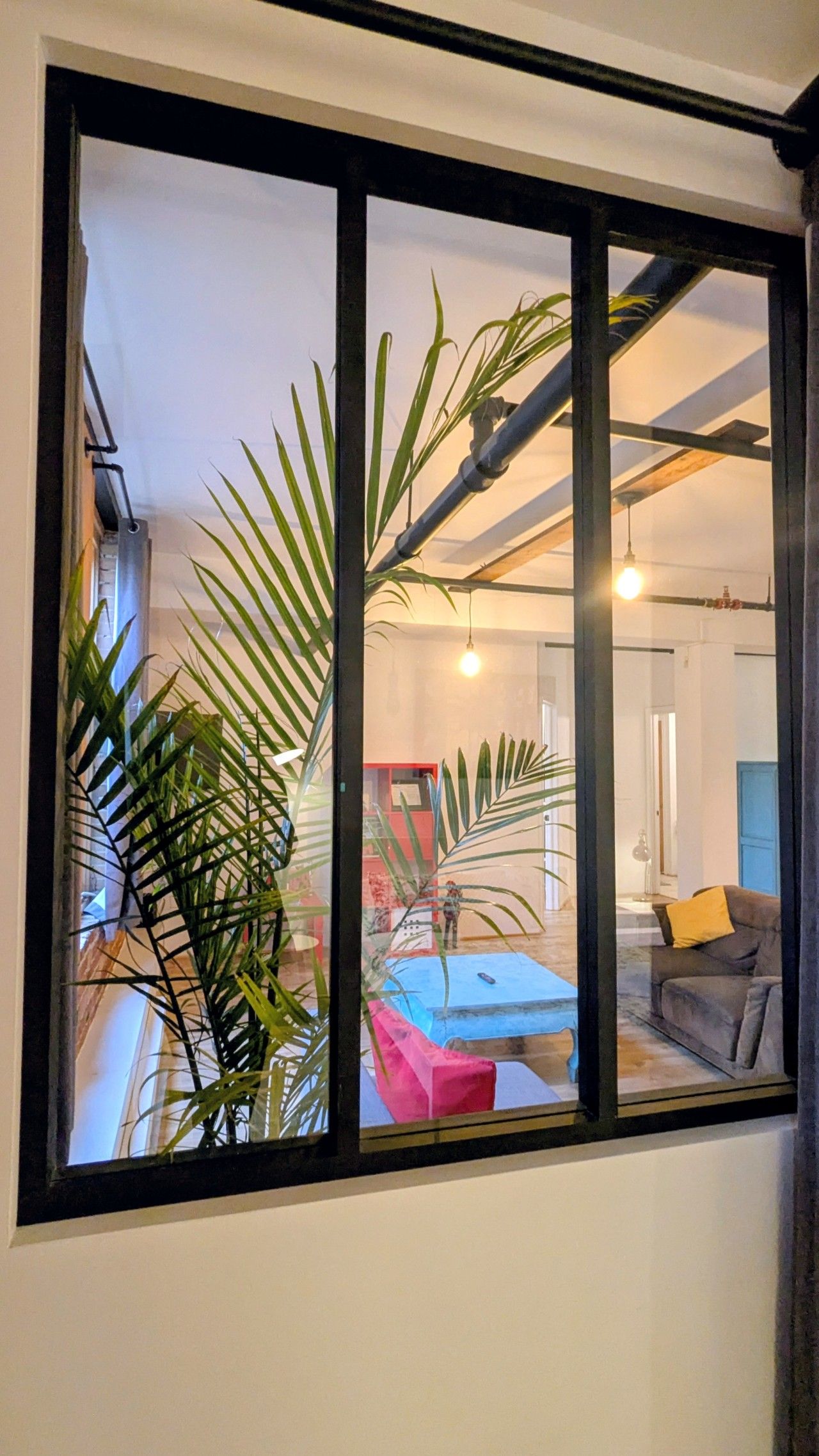 A room with a large window, a sofa, a table, and a plant.