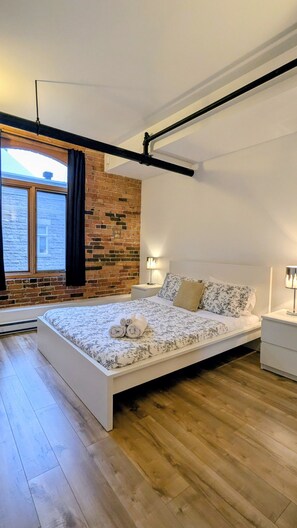 A modern bedroom with a large bed, a brick wall, and a window. - Saint-Roch neighbourhood with indoor parking (Québec)