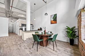Eine moderne Küche mit weißen Schränken, einem Essbereich mit einem runden Holztisch und einer Wand mit Ziegelverkleidung.