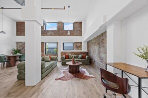 A spacious loft with exposed brick walls, a dining area, and a seating area with a central coffee table. - The Garden Loft Near NYC + Parking + Patio (Kearny)