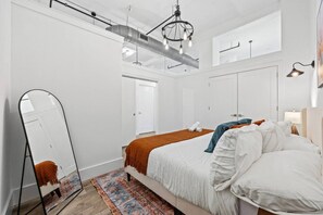 Ein modernes Schlafzimmer mit einem Bett, einem großen Spiegel, einer Pendelleuchte und einem gemusterten Teppich.