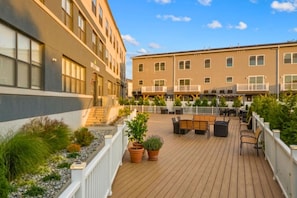 Ein Hotelinnenhof mit Außenplätzen, einer Holzterrasse und einem Gebäude mit mehreren Balkonen.