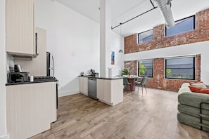 A modern apartment with a kitchen, dining area, and a loft bedroom with a brick wall. - The Garden Loft Near NYC + Parking + Patio (Kearny)