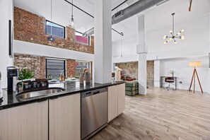 A modern kitchen with a large island, exposed brick walls, and a view to the living area. - The Garden Loft Near NYC + Parking + Patio (Kearny)