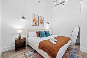 Ein modernes Schlafzimmer mit einem Bett, Nachttischen, einer Stehlampe, Wandbildern und einem Spiegel.