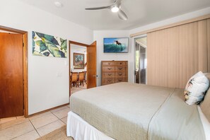 A bedroom with a bed, a dresser, a television, and artwork on the wall. - Makolea#21: Steps from the Beach, Beautifully Appointed 2 bedroom condo (KAILUA KONA)