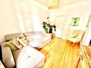 Un salon avec un canapé, un fauteuil, un plancher en bois et une porte.
