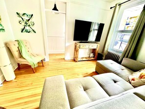 Un salon avec un canapé, un fauteuil, un téléviseur et des œuvres d’art accrochées au mur.