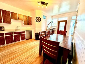 Une cuisine avec des meubles de rangement en bois, une table à manger avec des chaises et une horloge au mur.