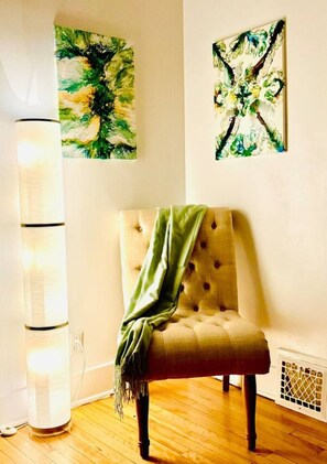 Une pièce comprenant un fauteuil à capitons, un lampadaire et deux tableaux abstraits accrochés au mur.