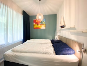 A bedroom with a bed, a hanging light fixture, a painting, and a sailboat decoration. - Holiday Home With 1 Bedroom (Westkapelle)