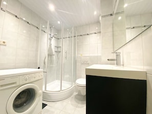 A modern bathroom with a glass-enclosed shower, a toilet, and a washing machine. - Holiday Home With 1 Bedroom (Westkapelle)