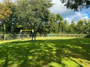 A grassy outdoor area with a swing set and a fenced play area. - Holiday Home With 1 Bedroom (Westkapelle)