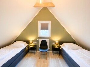 A triangular room with two beds, a chair, and two bedside tables with lamps. - Ok20 Holiday Home Oostkapelle (Oostkapelle)