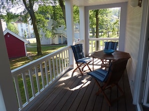 Eine überdachte Veranda mit einem Holztisch und zwei Stühlen, ein rotes Gartenhaus im Hintergrund und ein weißer Zaun.