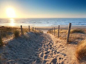 Ein sandiger Küstenweg führt zum Meer, begleitet von einer seitlichen Umzäunung.