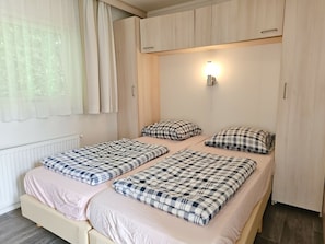 Ein Schlafzimmer mit zwei Betten, einem Fenster mit Vorhängen, einer Wandleuchte und einer Heizung.