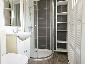 Ein modernes Badezimmer mit einer Duschkabine aus Glas, einem weißen Waschbecken und einer integrierten Ablage.