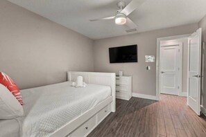 A bedroom with a bed, a nightstand, a TV mounted on the wall, and a door. - Seaglass Villa - Heated Pool - 5 br - 3 ensuite (St. Augustine)