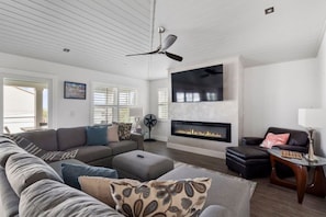 A modern living room with a fireplace, a ceiling fan, and a large TV mounted on the wall. - Seaglass Villa - Heated Pool - 5 br - 3 ensuite (St. Augustine)