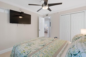 Ein Schlafzimmer mit Deckenventilator, Flachbildfernseher, Bett mit Blumenmuster auf der Bettwäsche und einem Kleiderschrank.