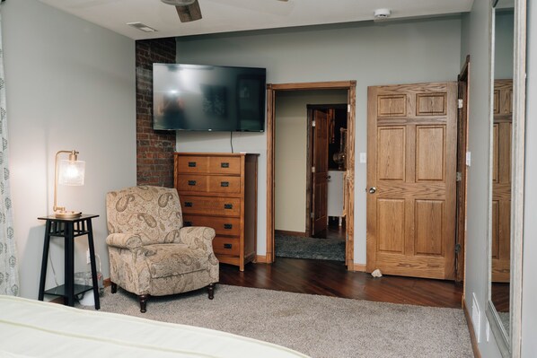 A bedroom with a bed, a chair, a dresser, a television, and a wooden door.