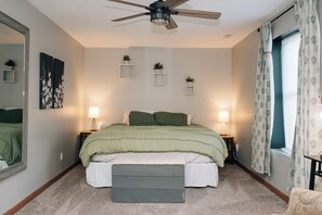 A bedroom with a bed, two bedside lamps, a ceiling fan, a window with curtains, and a mirror on the wall.