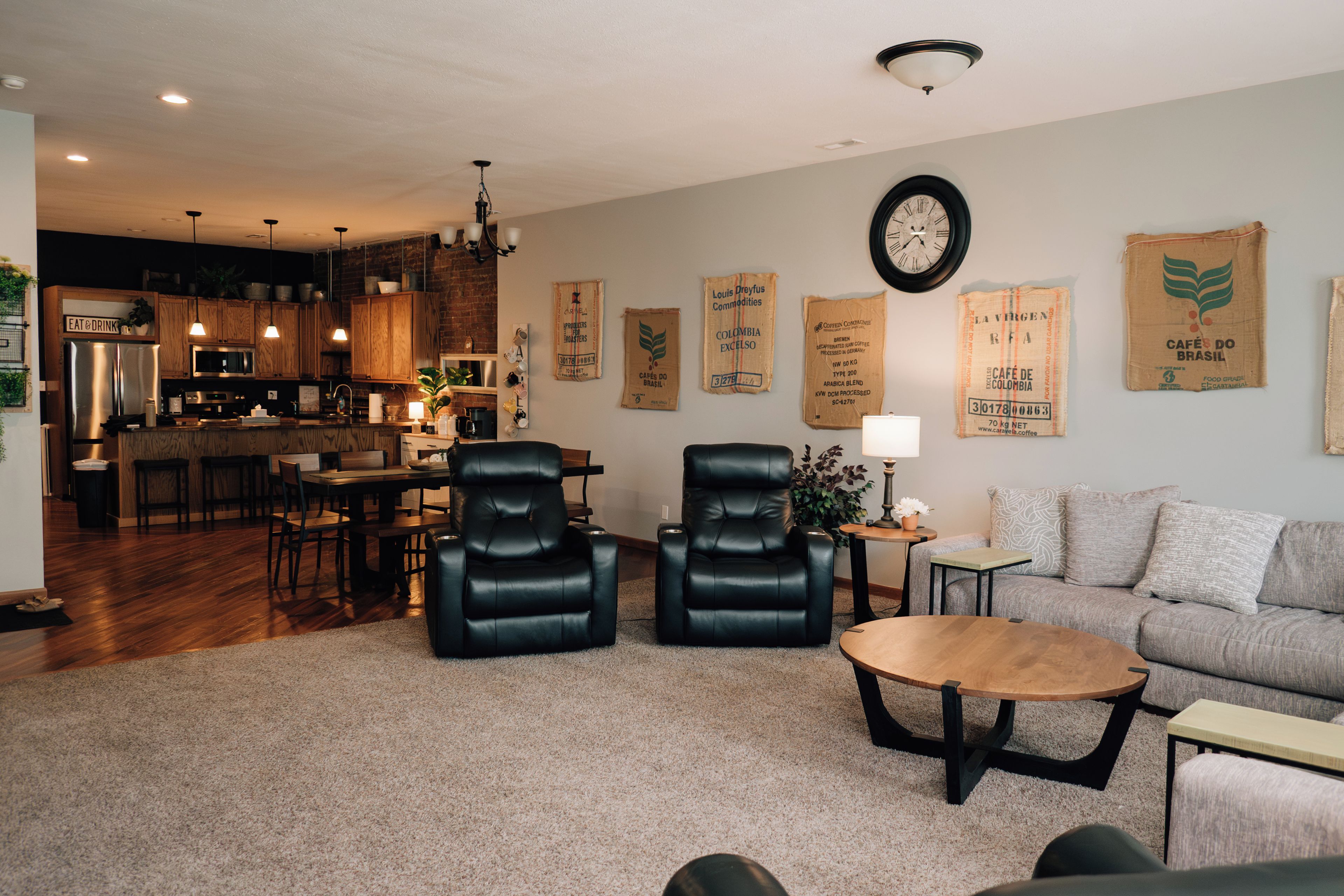 A modern living room with a sofa, two black leather chairs, a coffee table, and a dining area with a kitchen in the background.
