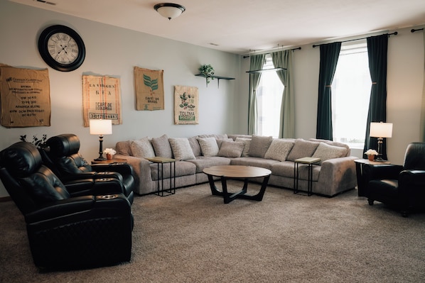 A living room with a sectional sofa, two armchairs, a coffee table, and a wall clock.