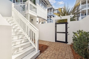 A white building with a staircase, a black gate, and a number '76' on the wall. - Stepping Stone Carriage House (Panama City Beach)