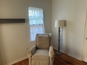 A room with a beige armchair, a floor lamp, a window with sheer curtains, and a white wall with vertical paneling. - Georgia’s cottage within walking distance to Texas Tech University. (Lubbock)