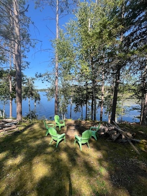 A lakeside campsite with green chairs and a fire pit.