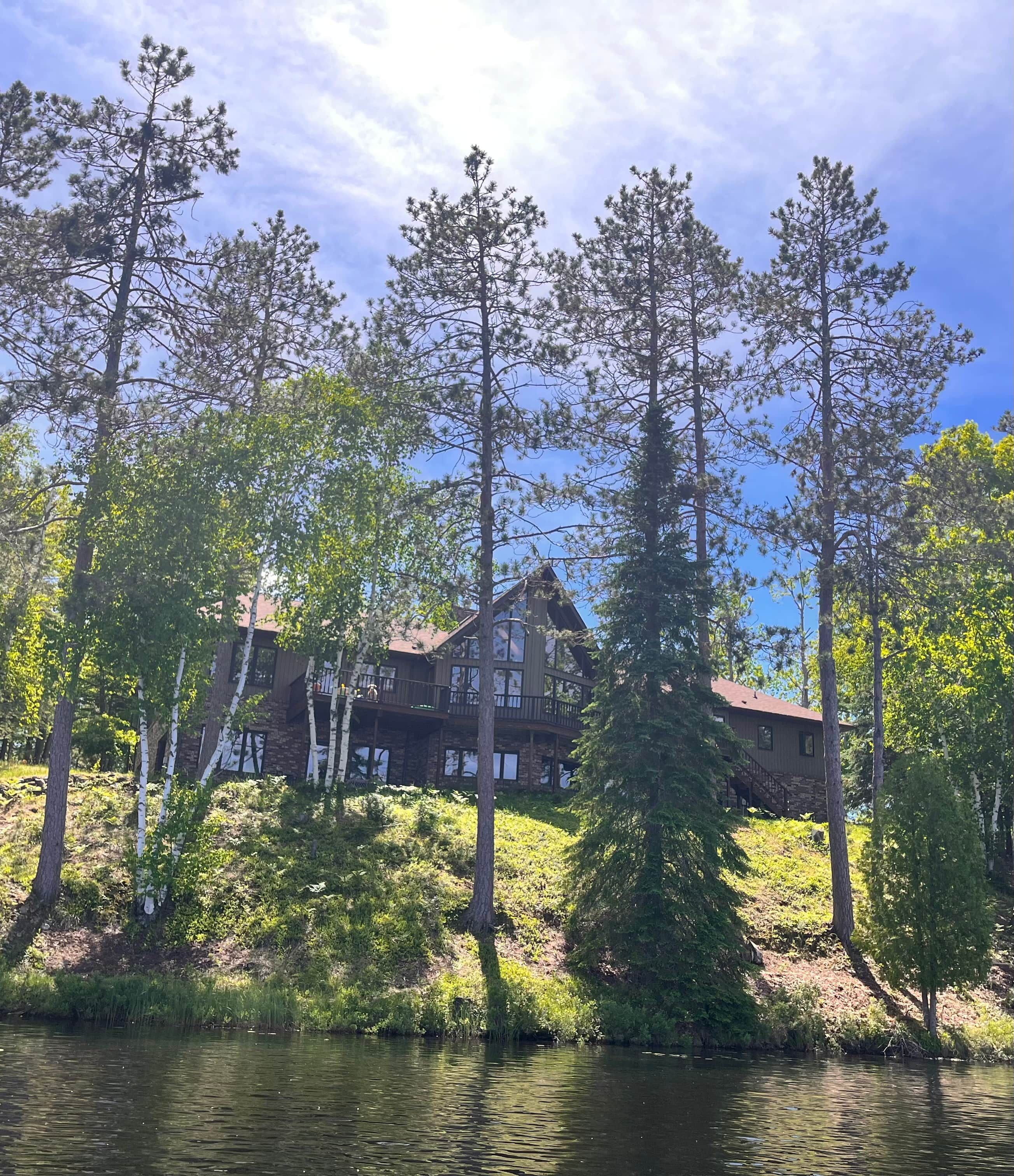 Una cabaña con fachada de madera, varios balcones y vistas a un lago rodeado de árboles.