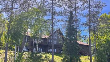 Una cabaña con fachada de madera, varios balcones y vistas a un lago rodeado de árboles.