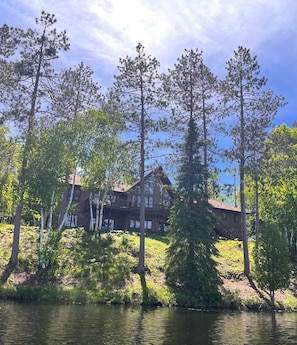 A lodge with a wooden exterior, multiple balconies, and a view of a lake surrounded by trees.
