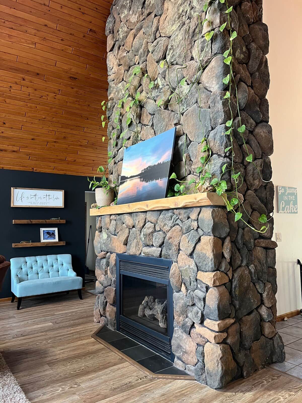 Una chimenea de piedra con un cuadro enmarcado encima, un sofá azul y un techo de madera.