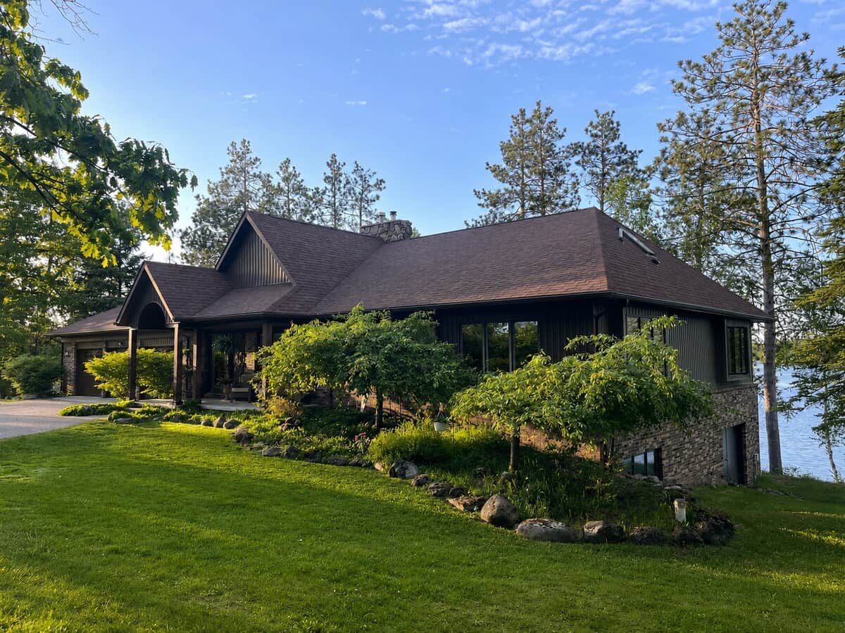 A two-story house with a stone facade, a covered porch, and a view of a lake.