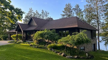 A two-story house with a stone facade, a covered porch, and a view of a lake.