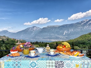 A table set with breakfast items, a view of mountains, and a clear sky. - Casa Runsel Bonassi (Tignale)