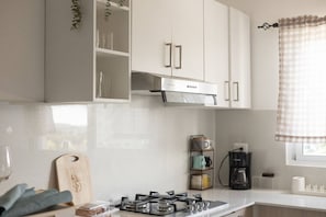 Eine moderne Küche mit weißen Schränken, einem Gasherd, einer Kaffeemaschine und einem Fenster mit kariertem Vorhang.