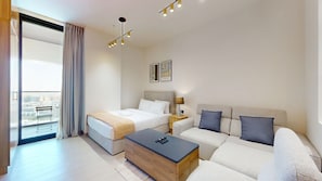 A modern hotel room with a bed, sofa, and a balcony with a view. - Studio in JVC near Circle Mall l Pool & Gym (Jumeirah Village Circle)